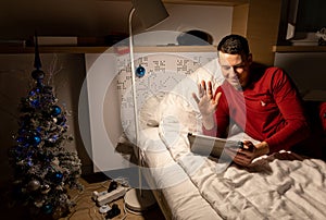 young man in christmas pyjama in bed watching a tablet