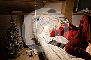 young man in christmas pyjama in bed watching a tablet