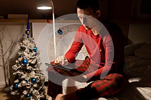 young man in christmas pyjama in bed watching a tablet