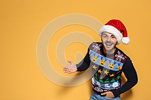 Young man in Christmas sweater and hat on color background