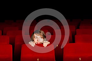 Young man in the cinema hiding behind a chair