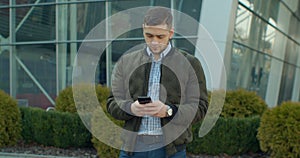 Young man at the city street using mobile phone, typing text, chatting with friends, man using cellphone outdoors.