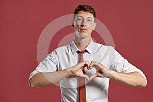 Young man in a classic white shirt and red tie posing over a pink background.