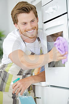 Young man cleaning oven in kitchen