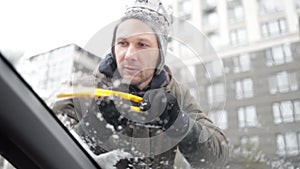Young man cleaning snow from car windshield outdoors on winter day.