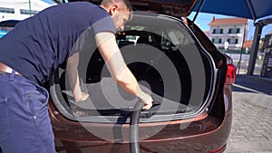 Young man cleans car inside with vacuum cleaner at self service car wash station