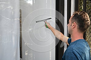 A young man cleans and polishes windows with a sponge