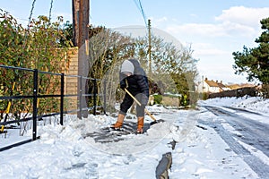 A young man clearing the footpath of snow and ice to make it safe to walk on during a heavy snowfall. Winter safety, clearing snow
