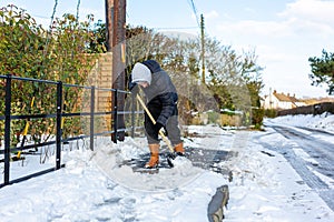 A young man clearing the footpath of snow and ice to make it safe to walk on during a heavy snowfall. Winter safety, clearing snow