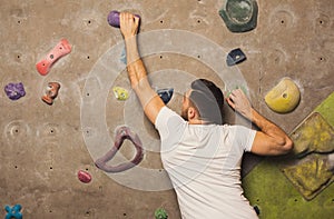 Young man climbing artificial rock wall at gym