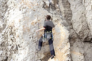 Young man climbing on a limestone wall with wide valley on the background