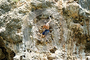 Young man climbing on a limestone wall with wide valley on the background