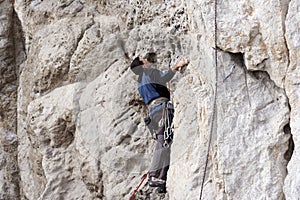 Young man climbing on a limestone wall with wide valley on the background