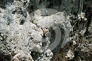 Young man climbing on a limestone wall with wide valley on the background