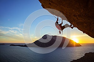 Young man climbing overhanging cliff at sunset