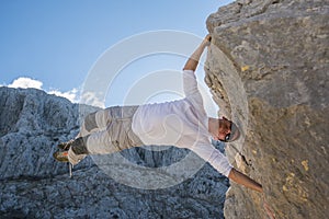 Young man climbing rock wall and hanging above gap