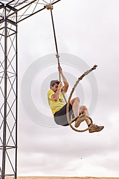Young man climbing a rope of knots in a Spartan race
