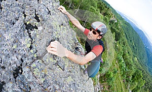 Young man climbing on a wall with green valley on the background