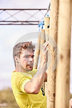 Young man climbing wooden sticks in a Spartan race - Extreme sports concept