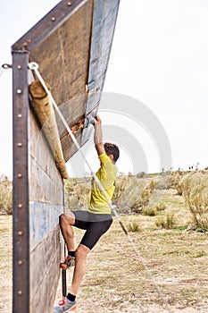 Young man climbing a wooden wall in a Spartan race