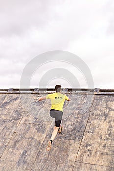 Young man climbing a wooden wall in a Spartan race