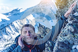 A young man climbs the mountain to the top and talking holding the phone. Concept of persistence and goal achievement