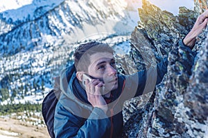 A young man climbs the mountain to the top and talking holding the phone. Concept of persistence and goal achievement