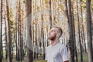 Young man with closed eyes enjoying the nature during a walk or jogging in the forest.