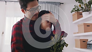 Young man closing eyes of his girlfriend and giving her bouquet of red roses. Happy Valentines day