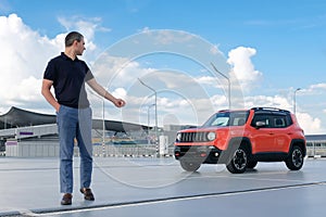 Young man closing his car with a remote control key in the parking.