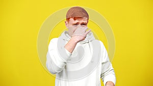 Young man closing nose smelling unpleasant smell. Middle shot portrait of Caucasian millennial guy at yellow background