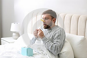 Young man with clothespin suffering from runny nose in bed indoors