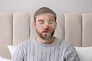 Young man with clothespin suffering from runny nose in bed indoors