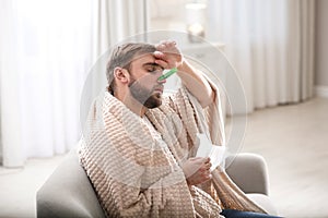 Young man with clothespin suffering from runny nose in room