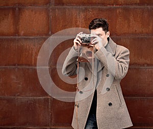 The young man in a coat photographs model the vintage camera at a metal rusty wall