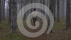 A young man in a coat runs through a foggy forest