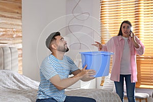Young man collecting leaking water from ceiling while his girlfriend calling roof repair service