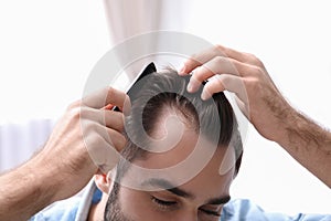 Young man with comb indoors. Hair loss problem