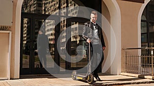 A young man comes out of the entrance of his house and holds an electric scooter