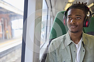 Young Man Commuting To Work Sitting On Train Streaming Music Or Podcast To Wireless Headphones