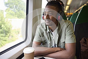 Young Man Commuting To Work Sitting On Train Wearing Wireless Headphones
