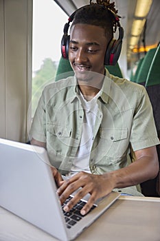 Young Man Commuting To Work Sitting On Train Working On Laptop Computer