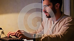 Young man at computer writing on paper sheet