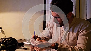 Young man at computer writing on paper sheet