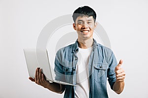 A young man, confident and happy, holds a laptop, giving a thumbs-up for success