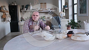 a young man with congenital mental disabilities is engaged in clay modeling sitting at home at a large table.