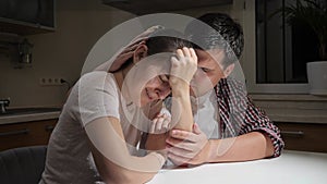 Young man consoling and hugging his crying wife on kitchen at night. Concept of despair, stress, depression, anxiety