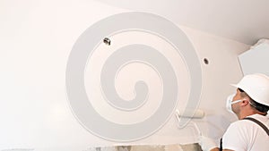 A young man in a construction helmet paints the walls in an apartment