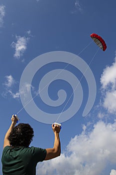 Young man controlling a red kite in the blue sky