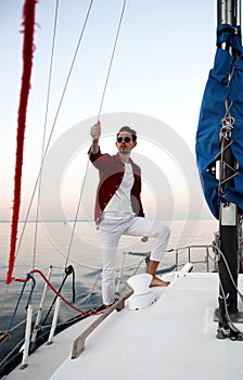 A young man controls a white sailing yacht. the captain of the sailing boat on board we meet the sunset.